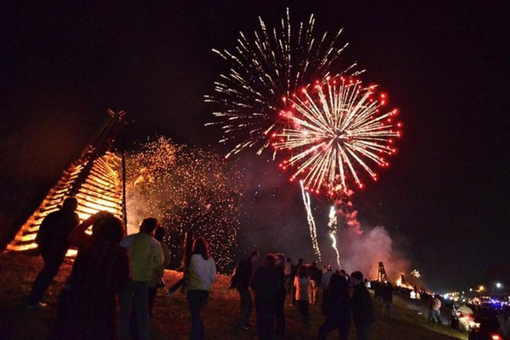 People watch fireworks and bonfire at night in a festive outdoor event.