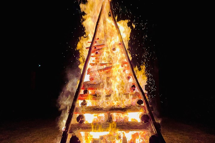 Large pyramid-shaped bonfire burning at night.
