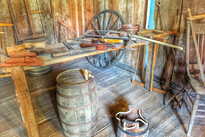 Old workshop with wooden tools, barrel, wagon wheel, and wooden walls.