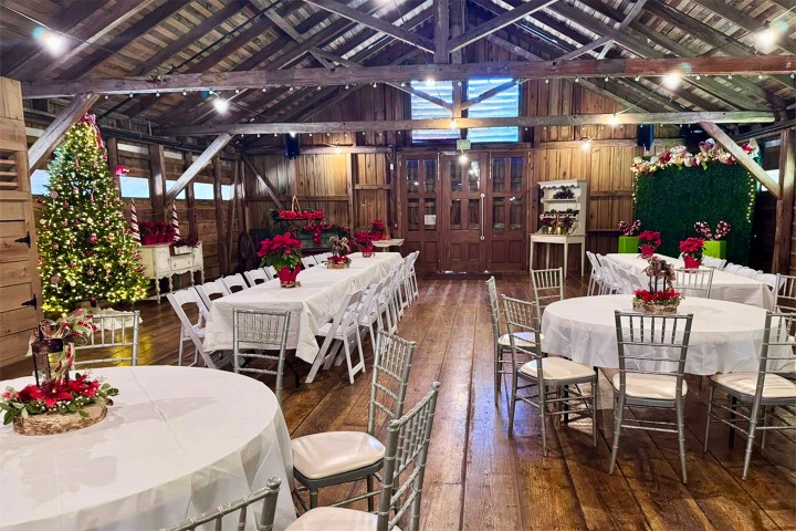 Festive barn interior with decorated tables, Christmas tree, and string lights.