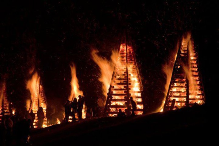 Silhouettes around large bonfires at night in pyramid shapes.