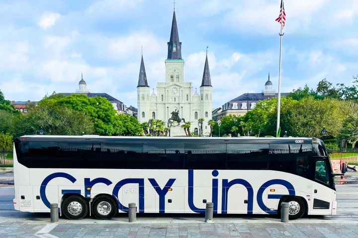 Tour bus parked in front of a cathedral with a statue in the foreground and a flag nearby.