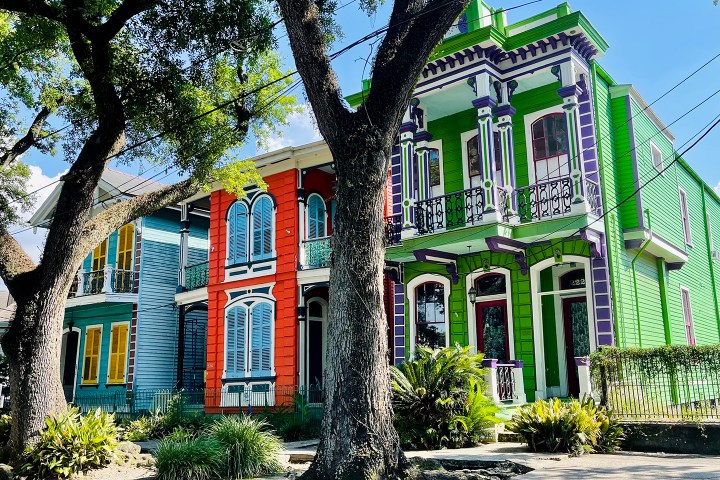Colorful Victorian houses in New Orleans, painted blue, red, and green, with trees in the foreground.