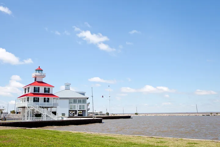 Lighthouse with red roof by a body of water under a blue sky with clouds.