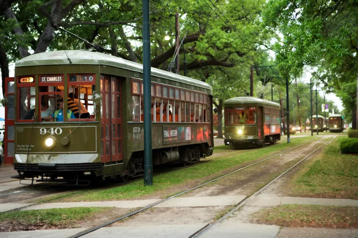 Streetcars on St. Charles Avenue line surrounded by trees in a green setting.