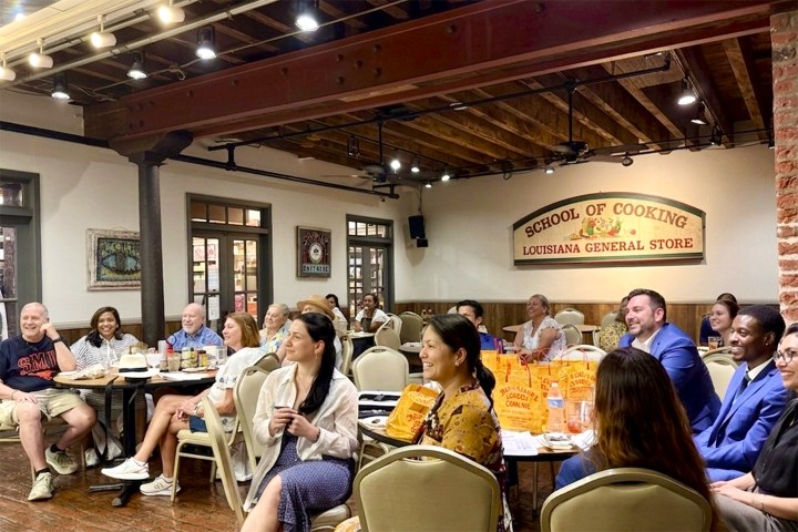People seated in a classroom at a cooking school with wooden beams and a sign on the wall.
