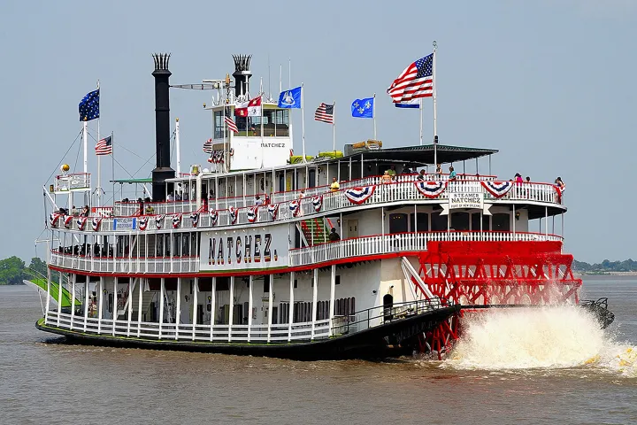Paddle steamboat Natchez with American flags and bunting on a river.