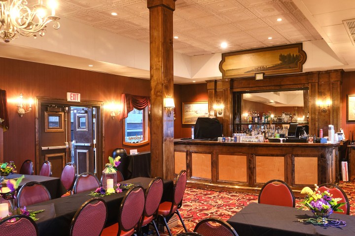 Elegant dining area with tables, chairs, chandelier, and a wooden bar with decor.