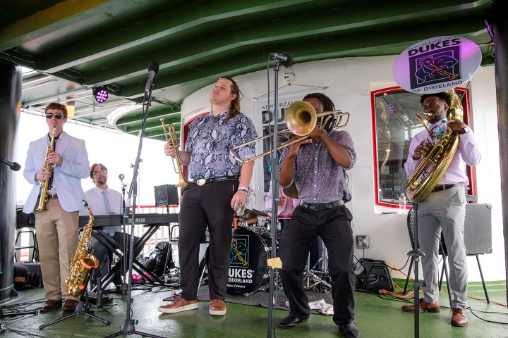 Five musicians playing on stage with saxophone, piano, trumpet, trombone, and tuba.