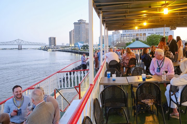 People socializing on a boat deck by a city riverfront during the evening.