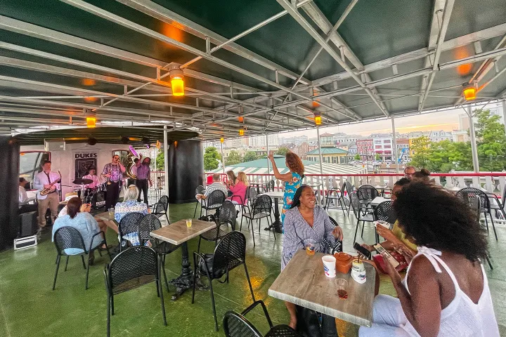 Outdoor deck with live band, people sitting and standing, enjoying music and drinks.