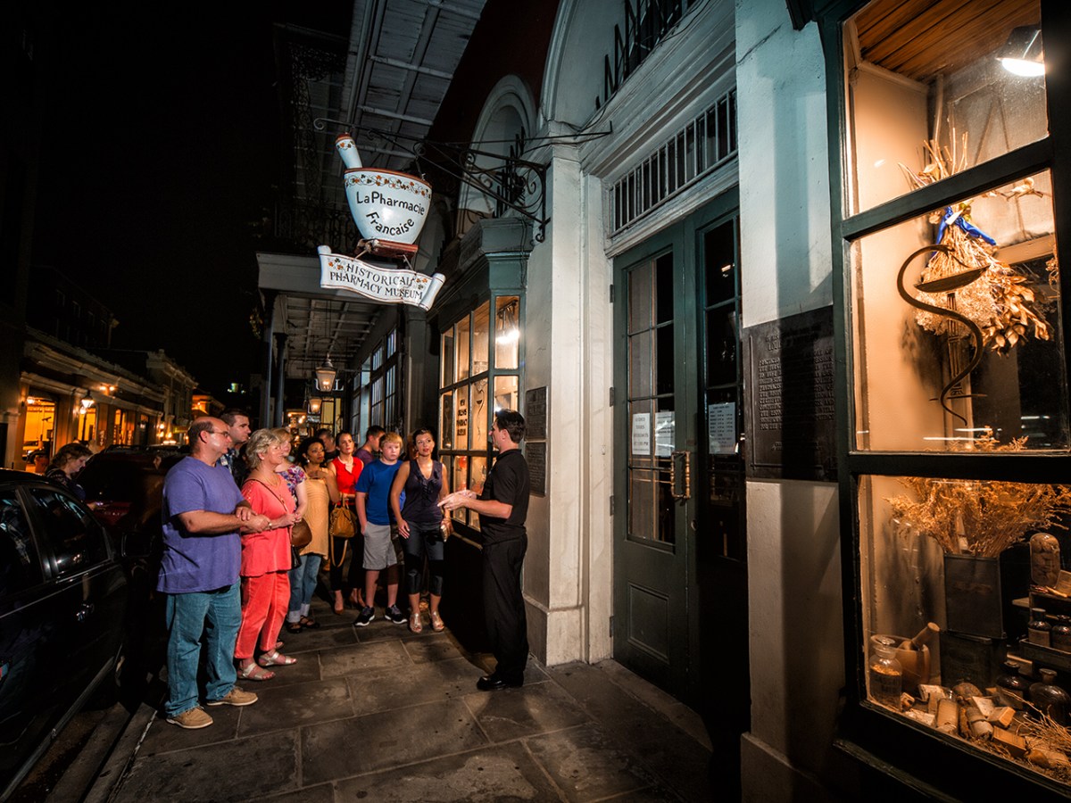 Group tour at night outside a historical pharmacy museum under a lit sign.