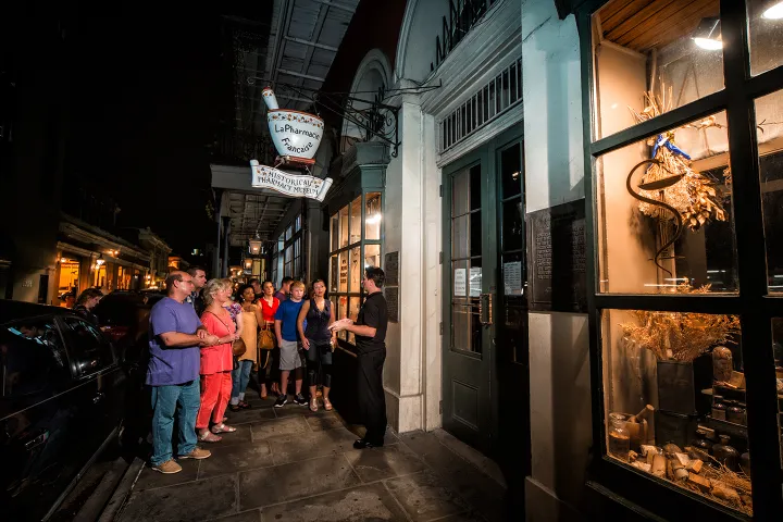 Group tour at night outside a historical pharmacy museum under a lit sign.