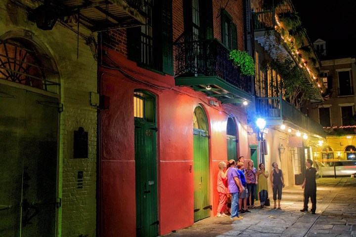 People gather on a brightly lit street with red and green doors at night.