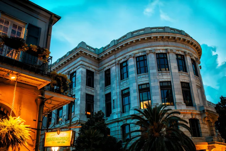 Two-story historic building with windows, lit by evening lights, under a blue sky.