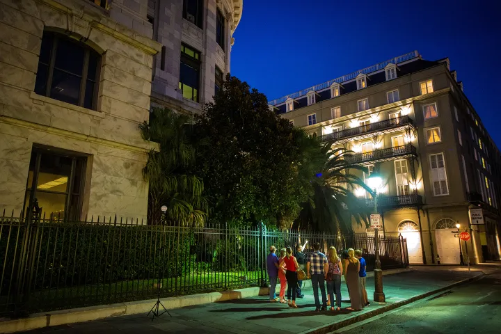 People gathered at night on a street corner near a tall building and palm tree.