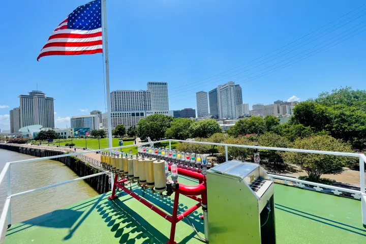 Boat deck with American flag, controls, and city skyline view.