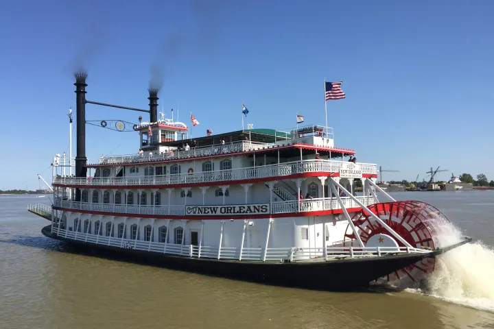 Steamboat with paddle wheel named New Orleans on a river, flags waving.