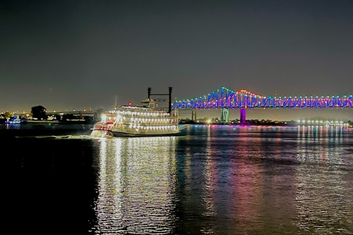 Illuminated riverboat and colorful lit bridge over water at night.