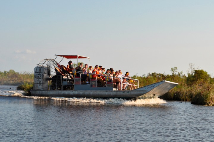 A group of people riding an airboat on a calm river with grassy banks.