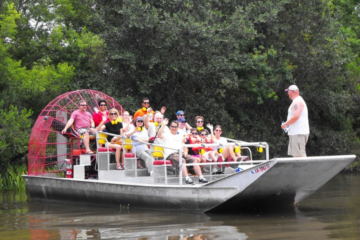 Group of people sitting in an airboat on a river with trees in the background.