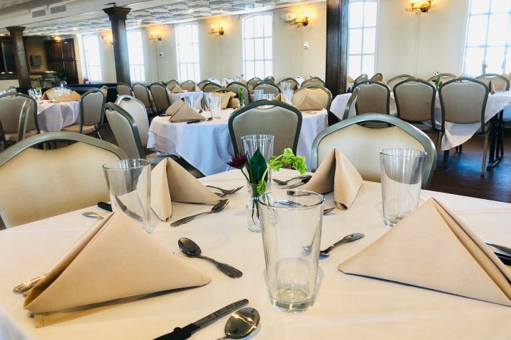 Indoor dining room with round tables set for a formal meal, napkins folded, and glasses on white tablecloths.