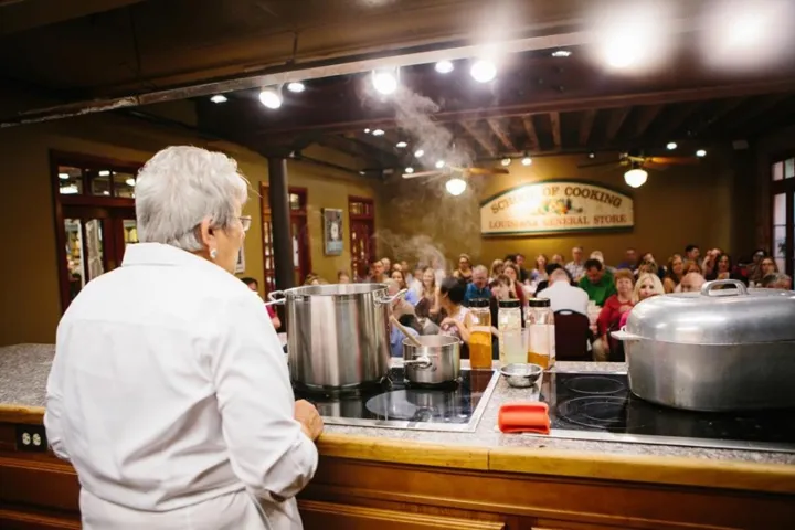 Chef cooking on stage with audience watching in a kitchen classroom.