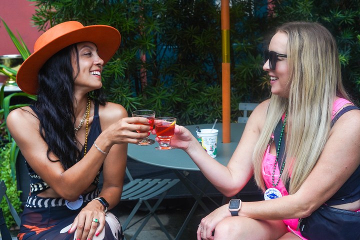 Two women sitting outside, smiling and toasting with drinks.