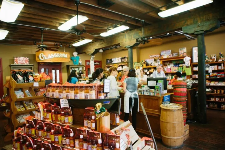 People shopping in a rustic store with wooden shelves and barrels, displaying various food items.