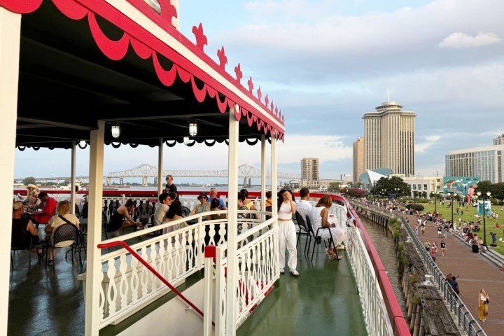 People on a docked riverboat with city skyline and bridge in background.