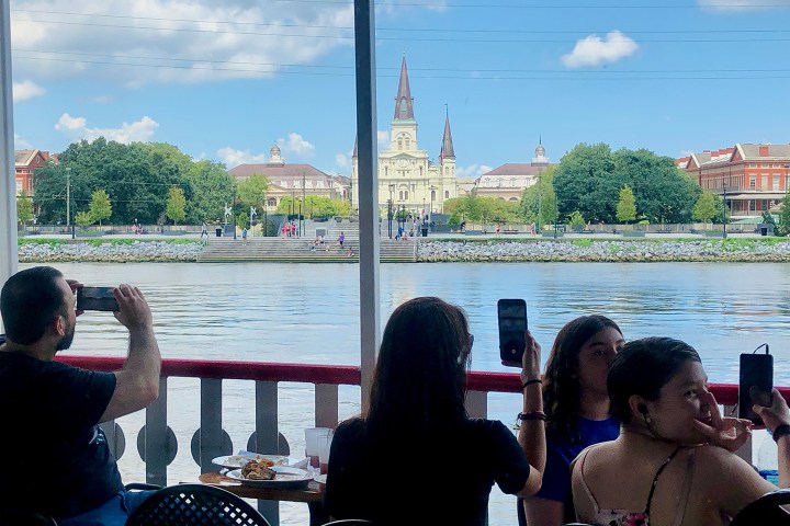 People on a boat taking photos of a riverside view with a cathedral in the background.