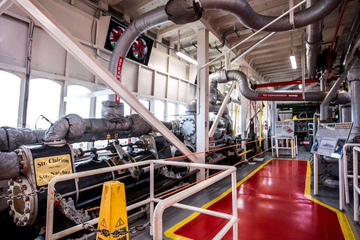 Interior view of a steam engine room with pipes and industrial equipment.