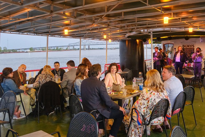 People dining on a covered deck with a river view and live band playing.