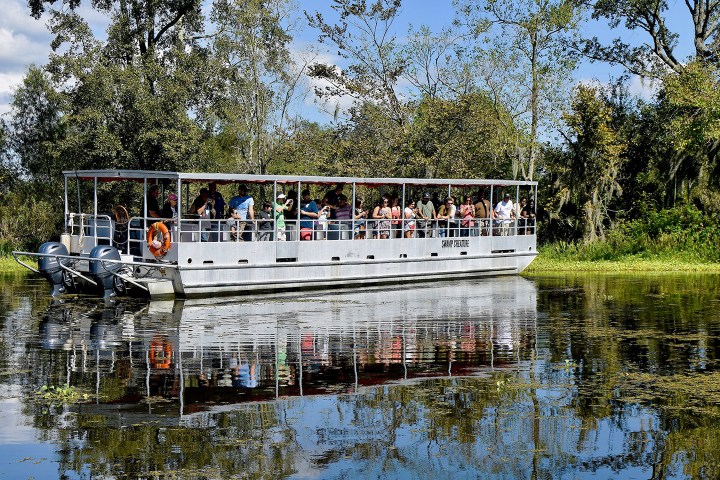Tour boat with passengers on a swamp, surrounded by trees and reflected in water.