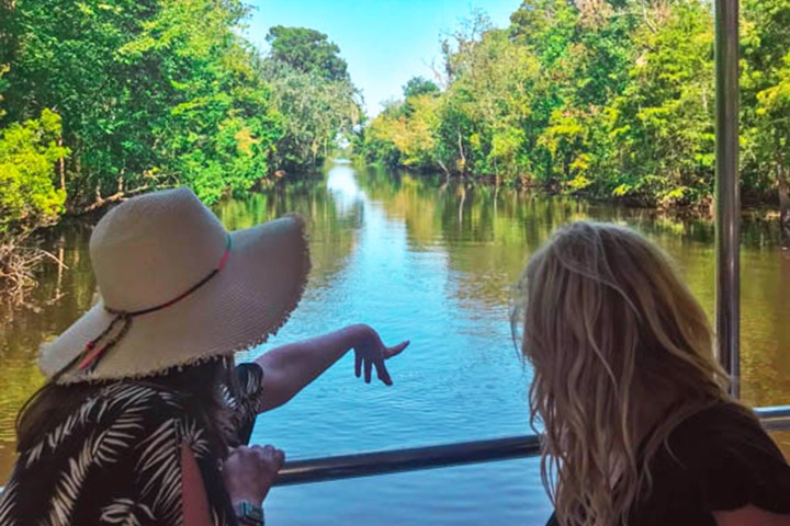 Two people on a boat, one pointing at a calm river surrounded by lush greenery.