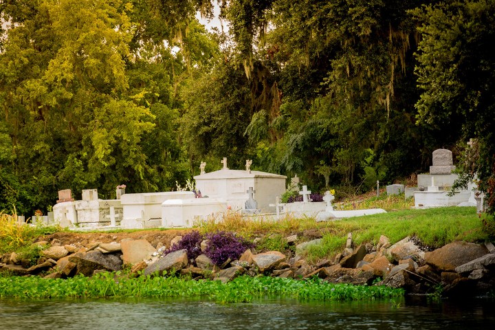 Graves and tombs surrounded by trees near a body of water.