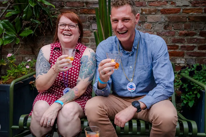 Two people sitting outside, laughing and holding drinks.