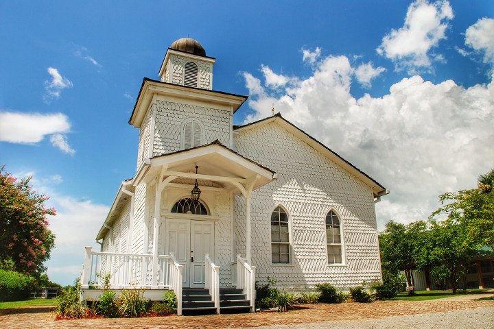 White wooden church with arched windows under a blue sky with clouds.