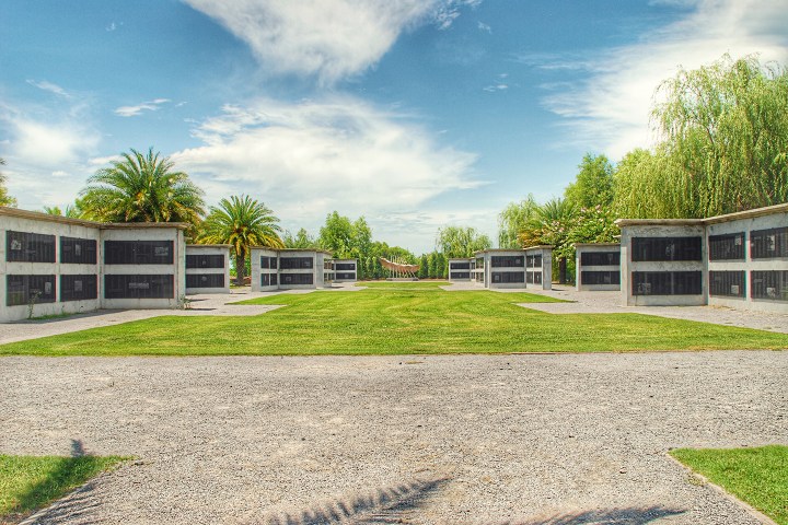Symmetrical cemetery with graves in niches, palm trees, under a cloudy sky.