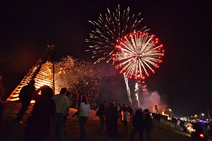 A crowd watching fireworks and bonfires at night.
