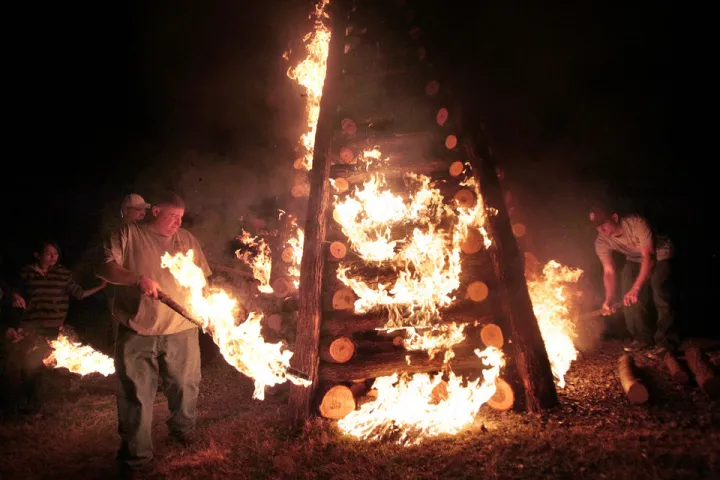 People lighting a large wooden structure on fire at night.