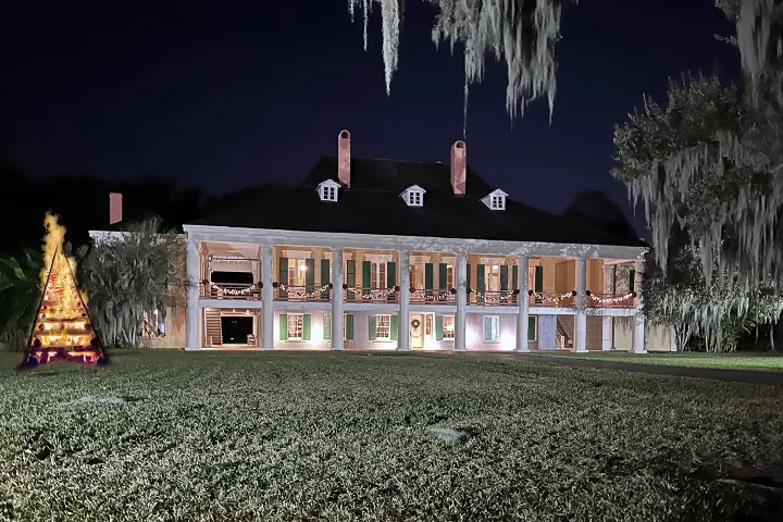Illuminated two-story mansion with Christmas lights and a decorated tree at night.