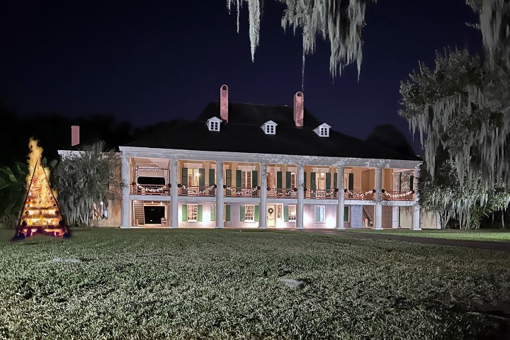 Lit-up mansion at night with Christmas decor and a bonfire on the left.
