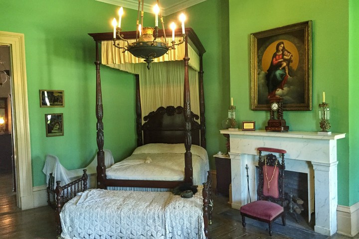 Vintage bedroom with canopy bed, green walls, chandelier, fireplace, and religious painting.