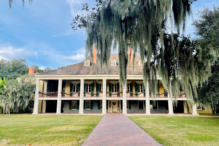 Historic two-story house with large columns and hanging Spanish moss trees.
