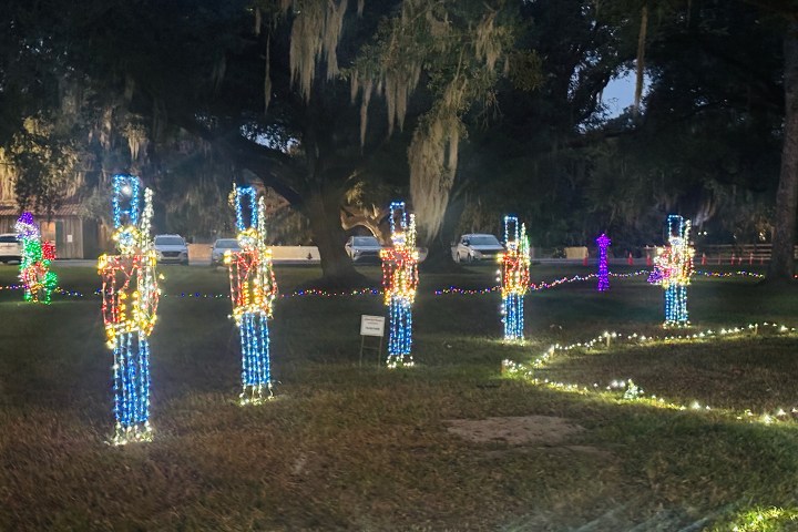 Six toy soldier light displays in a park at dusk.