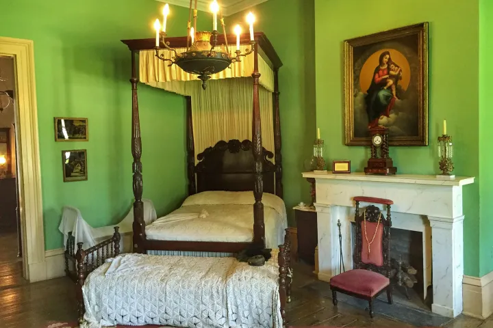 Vintage bedroom with canopy bed, green walls, chandelier, and fireplace with religious painting above.