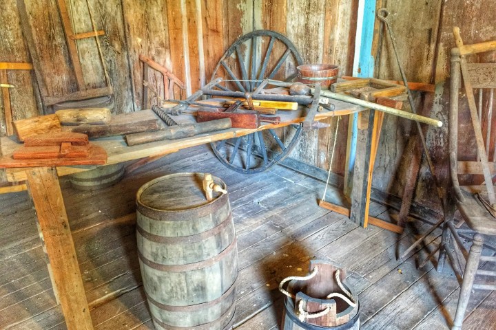 Old workshop with wooden tools, barrels, and a wagon wheel on a wooden floor.