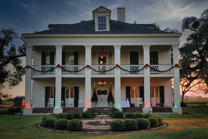 Colonial-style house with Christmas garlands and lights at sunset.