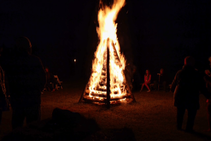 Large bonfire at night with people gathered around.